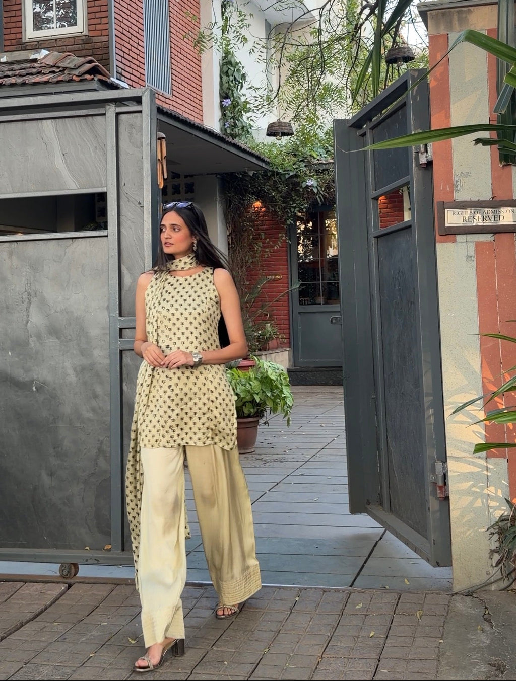 Woman in a patterned top and beige pants standing in front of a modern house.